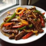 A close-up of tender Crock Pot Beef Fajitas served on a white plate with colorful saut&eacute;ed bell peppers and onions.