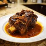 A single, rich, dark brown braised meat shank, likely veal or beef, served in a pool of tomato-based sauce, representing Easy Osso Buco.