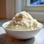 A white bowl filled high with freshly made cauliflower rice, ready for cooking or storage.