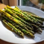 Close-up of perfectly Grilled Asparagus With Lemon Dressing, showing char marks and glistening seasoning on a white plate.