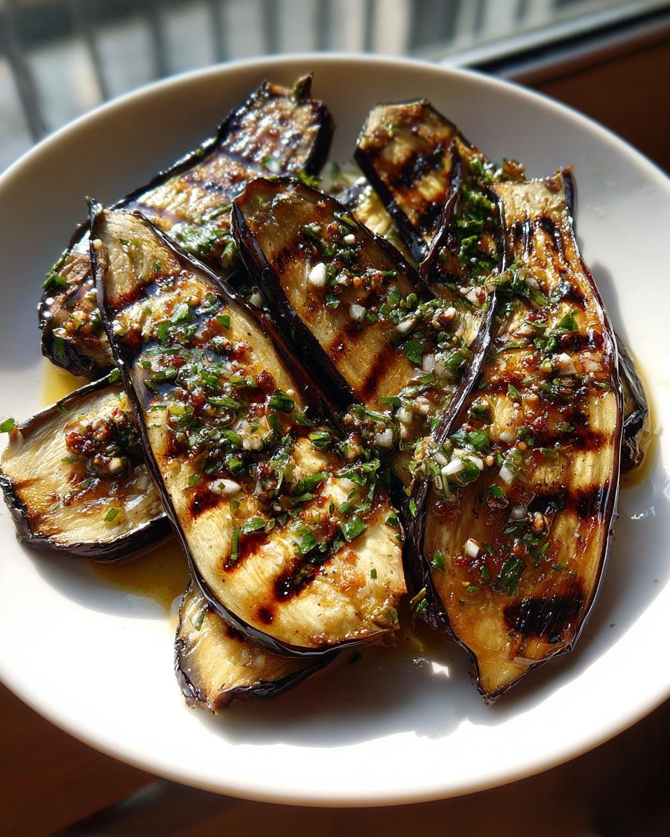 Close-up of grilled eggplant slices topped generously with garlic vinaigrette and fresh herbs.