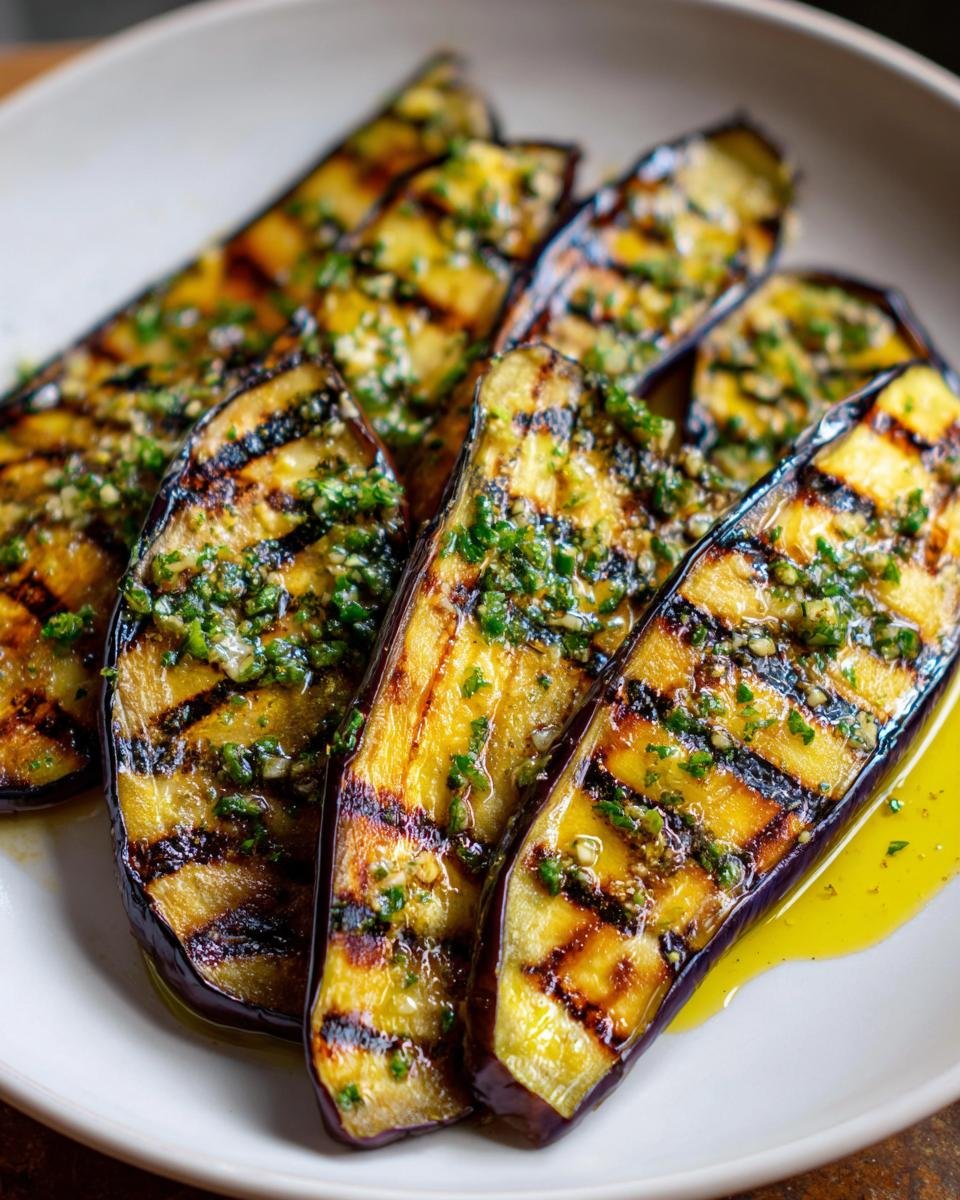 Close-up of several slices of perfectly Grilled Eggplant With Garlic Vinaigrette on a white plate.