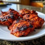 Close-up of several charred and vibrant red Piri Piri Chicken pieces served on a white plate.