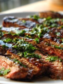 Close-up of perfectly grilled and sliced Mojo Carne Asada drizzled with a bright green herb sauce.