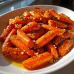 A close-up of glossy, roasted baby carrots coated in garlic, herbs, and oil, ready to serve as Parmesan Garlic Roasted Carrots.