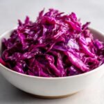 Close-up of bright, glossy shredded red cabbage slaw served in a small white bowl.