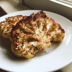 Two perfectly cooked Roasted Cauliflower Steaks seasoned with paprika, served on a white plate.