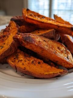 A close-up of perfectly caramelized Roasted Sweet Potato Wedges seasoned with herbs on a white plate.