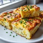 Four fluffy squares of baked Sheet Pan Eggs, topped with fresh chopped chives, served on a white plate.
