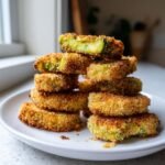A tall stack of golden brown, breaded Air Fryer Avocado Fries piled high on a white plate.