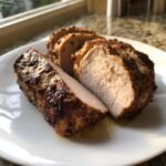 Close-up of sliced, seasoned Air Fryer Pork Tenderloin showing a moist, juicy interior on a white plate.