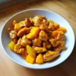 A white bowl filled with pieces of saucy Mango Chicken and chunks of fresh mango, ready to eat.