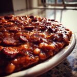 Close-up, glossy image of rich Baked Beans With Smoked Sausage served on a white plate.