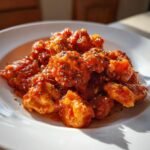 Close-up of bite-sized chicken pieces coated in vibrant Chicken Tomato Sauce and sprinkled with dried herbs.