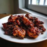 Close-up of crispy chicken pieces heavily coated in a dark, glossy Black Pepper Chicken sauce on a white plate.