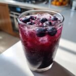 Close-up of a tall glass filled with icy Blueberry Agua Fresca, topped with fresh blueberries.