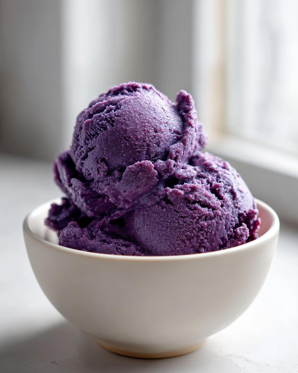 Two scoops of intensely purple Blueberry Nice Cream served in a small, light-colored bowl.