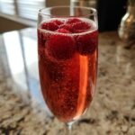 Close-up of a sparkling Chambord Bellini cocktail garnished with fresh raspberries in a flute glass.