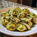 Close-up of a white bowl filled with Chicken Pesto Tortellini, featuring pasta coated in vibrant green pesto and chunks of shredded chicken.