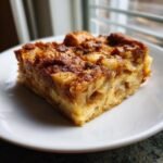 A close-up of a square slice of Cinnamon Apple French Toast Casserole on a white plate.