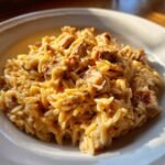 A close-up of creamy Cheesy Chicken Orzo pasta mixed with chunks of seasoned chicken, served in a white bowl.