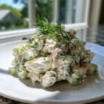 A generous scoop of Creamy Dill Chicken Salad mixed with celery, topped with fresh dill sprigs, served on a white plate.