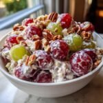 Close-up of a bowl of creamy Grape Salad featuring red and green grapes coated in dressing and topped with pecans.