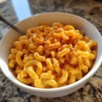 A close-up of creamy, cheesy Instant Pot Mac And Cheese topped with paprika in a white bowl.