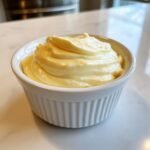 A close-up of thick, creamy Roasted Garlic Aioli swirled high in a small, white, fluted ramekin.