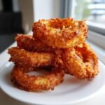 A close-up stack of golden brown, crispy air fryer onion rings piled on a white plate.