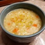 A close-up of a bowl of creamy Crock Pot Lemon Rice Soup, featuring rice, carrots, celery, and a lemon zest garnish.
