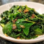Close-up of vibrant, glossy Garlic Butter Collard Greens topped with browned garlic bits in a white bowl.