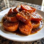 A close-up of thick-cut, glazed Candied Yams piled on a white plate, glistening with brown sugar syrup and spices.