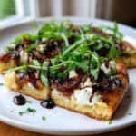 Close-up of a slice of Goat Cheese Pizza topped with caramelized onions, fresh arugula, and balsamic glaze.