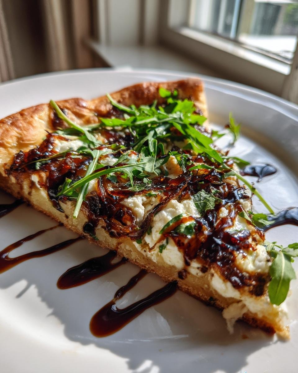A close-up slice of Goat Cheese Pizza topped with caramelized onions, fresh arugula, and drizzled with balsamic glaze.