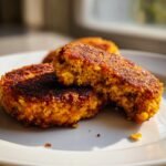 Close-up of golden brown Easy Chickpea Patties on a white plate, one patty is broken open showing the texture.