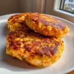 Three perfectly seared, golden brown Salmon Burgers stacked slightly on a white plate, garnished with fresh dill.
