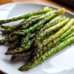 A close-up of bright green, perfectly seasoned Grilled Asparagus spears with slight charring on a white plate.