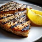 Close-up of two perfectly seasoned and charred Grilled Swordfish steaks served with lemon wedges on a white plate.