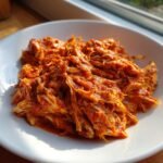 Close-up of shredded, saucy Instant Pot Chicken Tinga piled high on a white plate, illuminated by natural light.