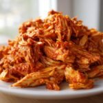 Close-up of a mound of saucy, shredded Instant Pot Chicken Tinga piled high on a white plate.
