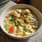 Close-up of a white bowl filled with Instant Pot Creamy Chicken Tortellini Soup, garnished with parsley.