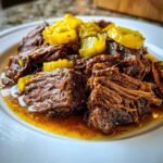 Close-up of shredded Instant Pot Mississippi Pot Roast served in its savory juices, topped with bright yellow pepperoncini rings.