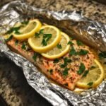 A cooked salmon fillet seasoned with herbs and topped with lemon slices in a foil packet.