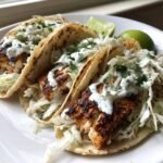 Close-up of three grilled Mahi Mahi Fish Tacos topped with slaw and white sauce, served with lime wedges.