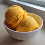 Three scoops of vibrant, bright orange Mango Sorbet served in a small white bowl.