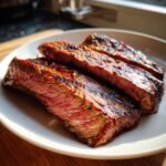 Close-up of three thick slices of medium-rare Marinated London Broil steak on a white plate.