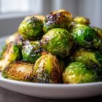 Close-up of a mound of perfectly caramelized Oven Roasted Brussels Sprouts on a white plate.