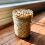 A jar of creamy Peanut Powder Overnight Oats topped with seeds and peanut butter.