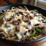 Close-up of a hot Philly Cheesesteak Skillet loaded with steak, peppers, mushrooms, and melted white cheese.